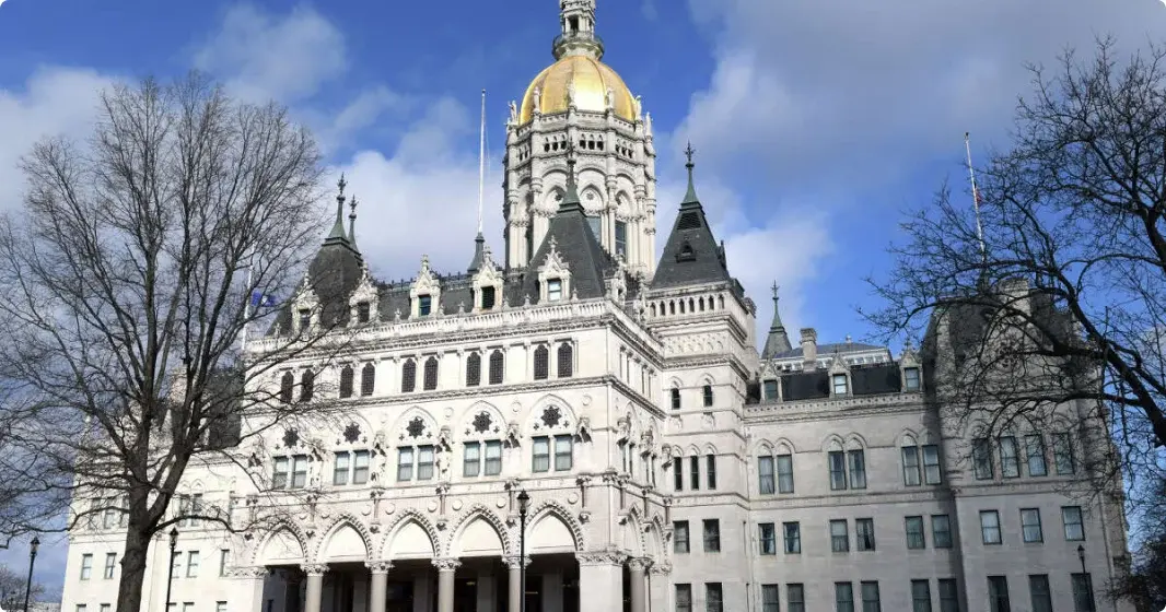 The CT state capitol building, with golden dome, is in front of a blue sky